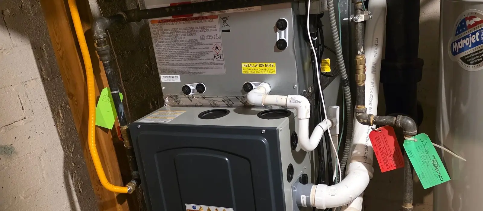 American Standard gas furnace and evaporator coil in a basement with a green approved-inspection tag hanging from the gas line