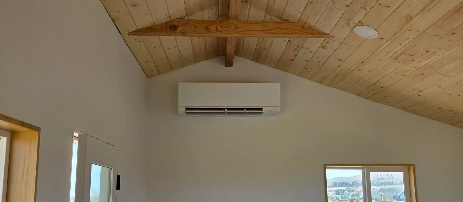 Mitsubishi Electric wall-mounted mini-split head installed high on a white wall beneath a vaulted cedar plank ceiling in a new Montana build