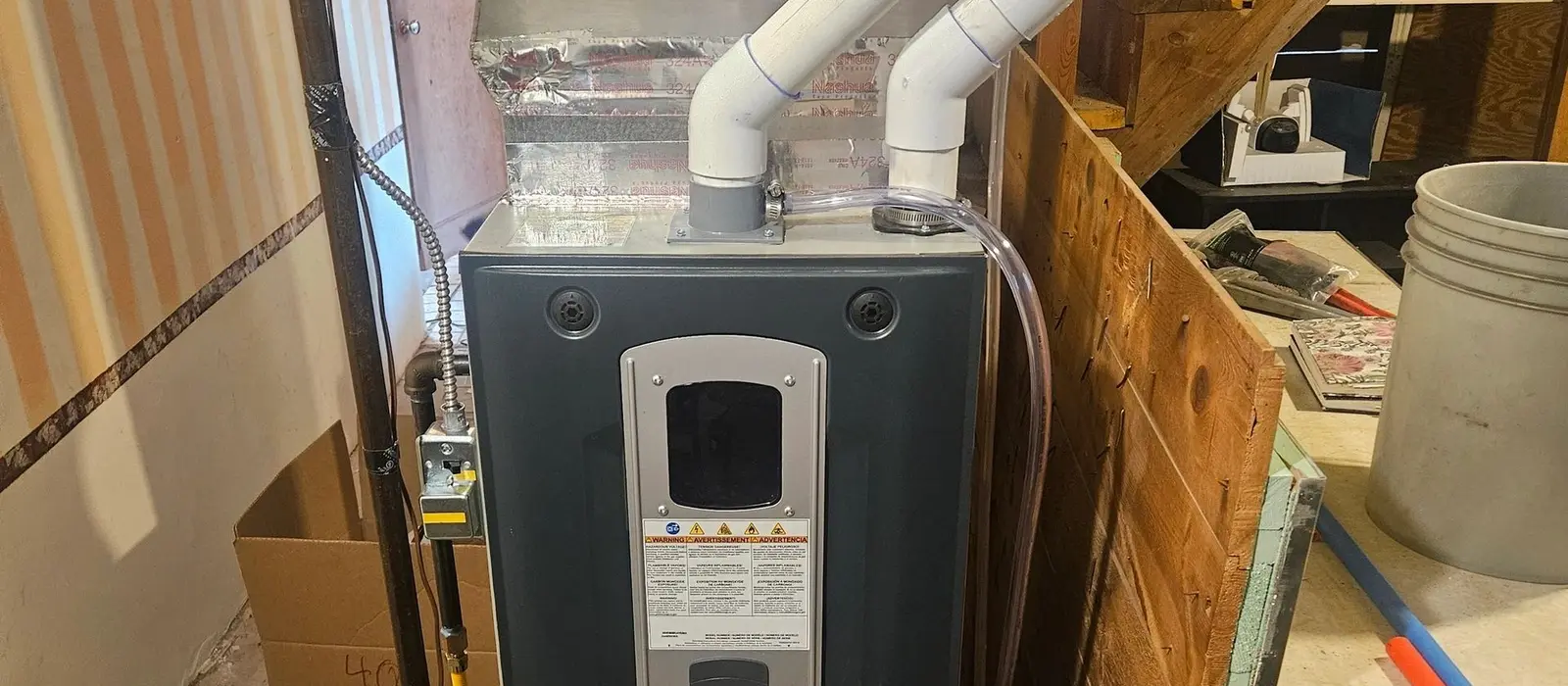High-efficiency American Standard gas furnace installed in a basement with twin white PVC intake and exhaust pipes elbowing up into the joists