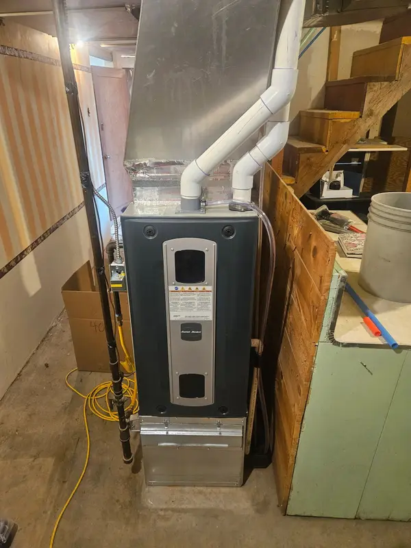 American Standard gas furnace installed in a basement with twin white PVC intake and exhaust pipes elbowing up into the joists and a condensate line run to the side