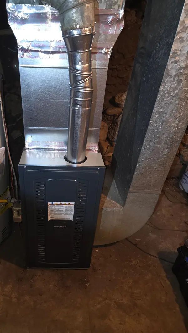 American Standard gas furnace with a new galvanized flue rising from the top plate into insulated ductwork above, installed alongside an existing water heater